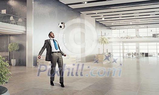 Businessman in suit in modern office jumping to hit soccer ball Businessman in suit in modern office jumping to hit soccer ball