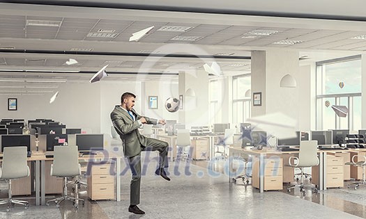 Businessman in suit in modern office jumping to hit soccer ball Businessman in suit in modern office jumping to hit soccer ball