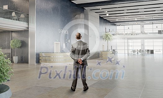 Thoughtful businessman standing with back in empty office