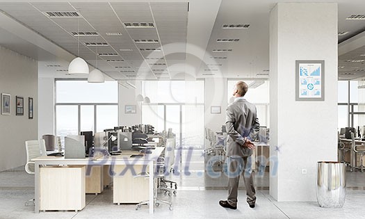 Thoughtful businessman standing with back in empty office Thoughtful businessman standing with back in empty office