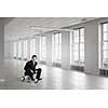 Young funny businessman riding three wheeled bicycle in office