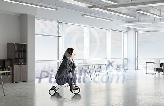 Young pretty businesswoman riding three wheeled bike in office Young pretty businesswoman riding three wheeled bike in office