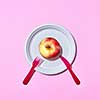Natural organic apple on a disposable plate served with plastic knife and fork on a pink background with copy space. Top view.