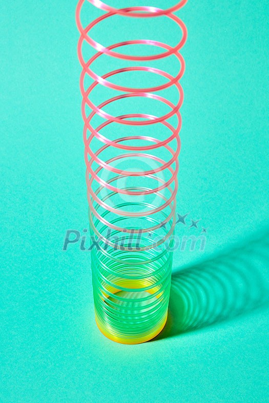 Multicolored slinky toy spiral with soft shadows on a pastel turquoise background, place for text. Multicolored slinky toy spiral with soft shadows on a pastel turquoise background, place for text.