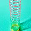 Multicolored slinky toy spiral with soft shadows on a pastel turquoise background, place for text.