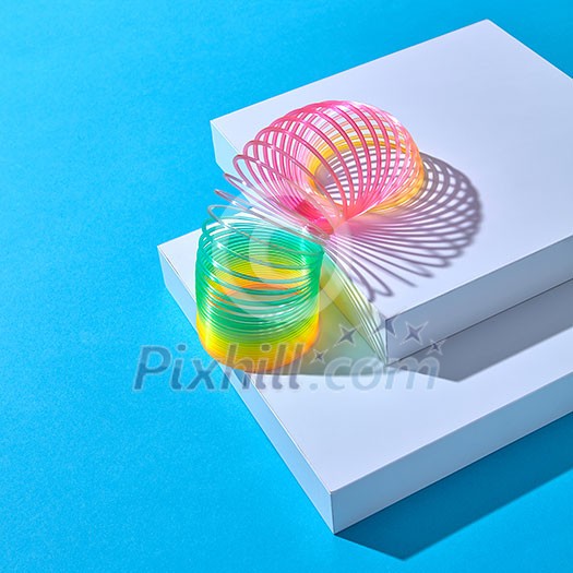 Rainbow plastic multicolored spring spiral goes down white stairs step by step on a pastel background with shadows, copy space. Rainbow plastic multicolored spring spiral goes down white stairs step by step on a pastel background with shadows, copy space.