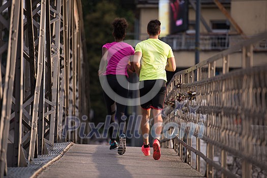 healthy young multiethnic couple jogging across the bridge in the city at early morning with sunrise in background