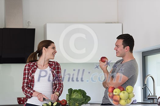 Young handsome couple in the kitchen beautiful woman preparing a salad while the man eating an apple Young handsome couple in the kitchen beautiful woman preparing a salad while the man eating an apple
