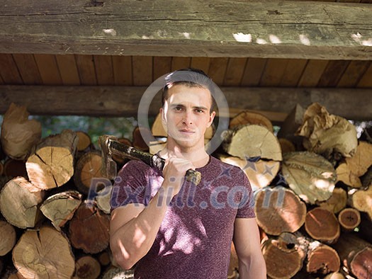 A handsome young man with an ax on his shoulder and lots of wood in the background A handsome young man with an ax on his shoulder and lots of wood in the background