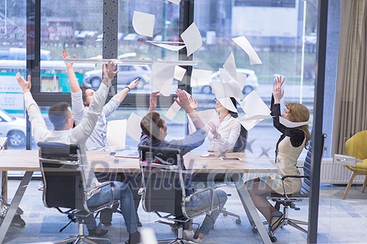 Group of young business people throwing documents and looking happy while celebrating success at their working places in startup office Group of young business people throwing documents and looking happy while celebrating success at their working places in startup office