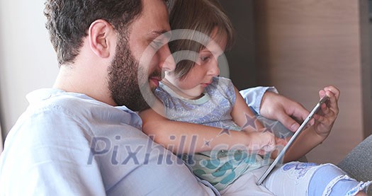 Father Daughter sitting in sofa playing games on tablet Father Daughter sitting in sofa playing games on tablet