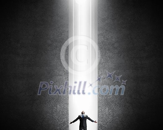 Businessman with hands spread apart standing in light coming from above Businessman with hands spread apart standing in light coming from above