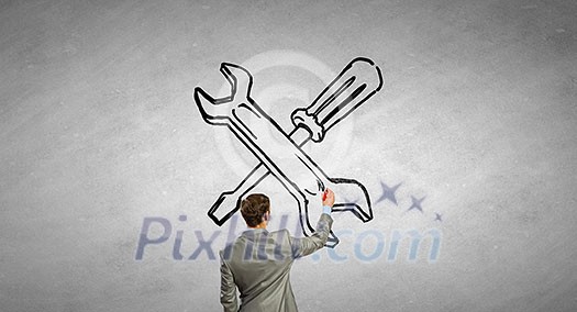 Rear view of businessman drawing tools on wall Rear view of businessman drawing tools on wall