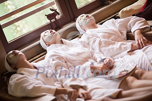 beautiful young women getting facial clay mask at spa, lying with cucumbers on eyes beautiful young women getting facial clay mask at spa, lying with cucumbers on eyes