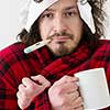 young Man with flu and fever wrapped holding cup of healing tea isolated over white