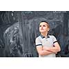 portrait of happy boy with orange wooden pen behind the ear standing in front of black chalkboard
