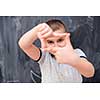 happy cute little boy having fun making hand frame gesture while standing in front of black chalkboard
