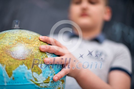 happy cute boy learning about the world using globe of earth while standing in front of black chalkboard happy cute boy learning about the world using globe of earth while standing in front of black chalkboard