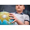 happy cute boy learning about the world using globe of earth while standing in front of black chalkboard
