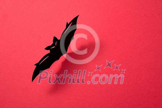Paper flying handcraft bat presented on a red background with a pattern of shadows and space for text. Mystic Halloween layout. Flat lay Paper flying handcraft bat presented on a red background with a pattern of shadows and space for text. Mystic Halloween layout. Flat lay