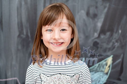 portrait of happy smiling cute little girl standing in front of black chalkboard portrait of happy smiling cute little girl standing in front of black chalkboard