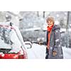 Pretty, young woman cleaning her car from snow after heavy snowstorm (color toned image)