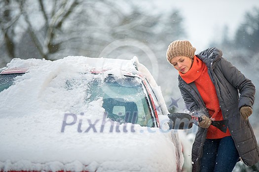 Pretty, young woman cleaning her car from snow after heavy snowstorm (color toned image)