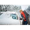 Pretty, young woman cleaning her car from snow after heavy snowstorm (color toned image)