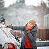 Pretty, young woman cleaning her car from snow after heavy snowstorm (color toned image)