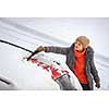 Pretty, young woman cleaning her car from snow after heavy snowstorm (color toned image)