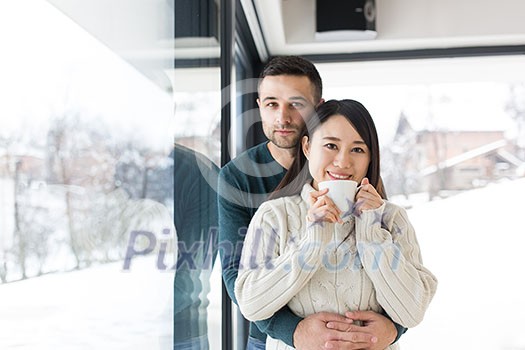 happy young multiethnic couple enjoying morning coffee by the window on cold winter day at home happy young multiethnic couple enjoying morning coffee by the window on cold winter day at home