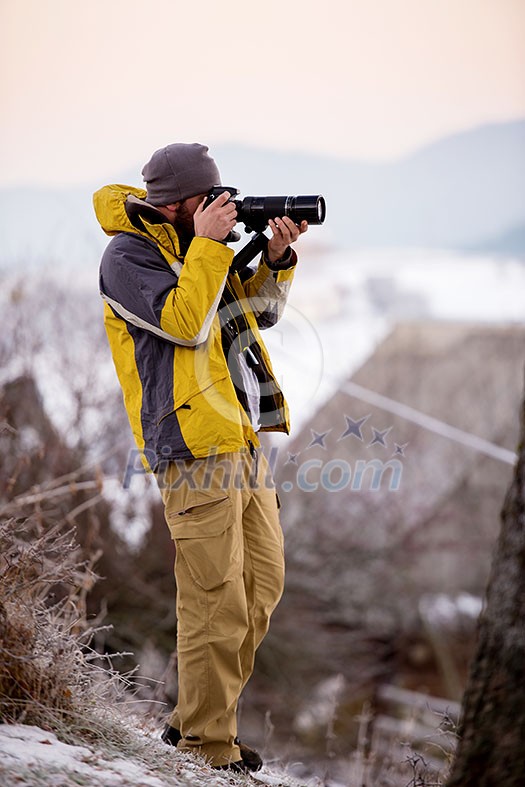 Young cheerful male photographer taking photographs of winter forest with digital camera at mountains Young man shooting photos outdoors Young cheerful male photographer taking photographs of winter forest with digital camera at mountains Young man shooting photos outdoors