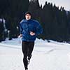 young  man jogging on snow in forest, bautiful sunny winter day. handsome sporty ahtlete man running
