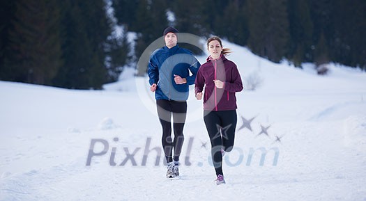 healthy young couple jogging outside on snow in forest. athlete running on beautiful sunny winter day healthy young couple jogging outside on snow in forest. athlete running on beautiful sunny winter day