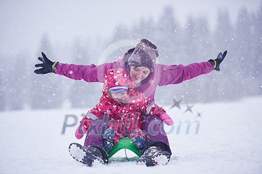 happy family on winter vacation, mom and cute little girl have fun and slide while snow falkes falling happy family on winter vacation, mom and cute little girl have fun and slide while snow falkes falling
