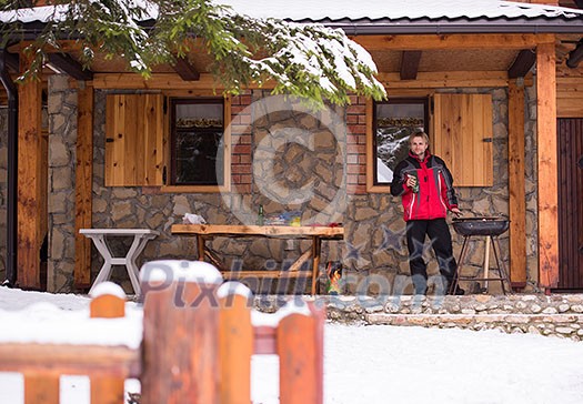 young man cooking meat on barbecue in front of the weekend house on a cold winter day young man cooking meat on barbecue in front of the weekend house on a cold winter day