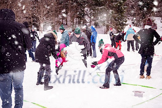 group of young happy business people having a competition in making snowmen while enjoying snowy winter day with snowflakes around them during a team building in the mountain forest