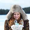 happy young redhair girl  with gift and snow in  hands. Christmas and winter shopping concept, forest in background