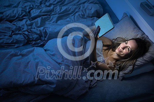 Pretty, middle-aged woman using her tablet computer before sleep in bed in the evening Pretty, middle-aged woman using her tablet computer before sleep in bed in the evening