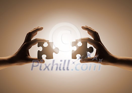 Close up of human hands connecting puzzle elements Close up of human hands connecting puzzle elements
