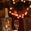 champagne and crystal glasses on a wooden table with candles and holiday lights in the background