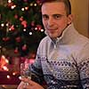 Portrait of a happy young man with a glass of champagne celebrating winter holidays at home beautifully decorated for Christmas