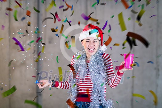 young happy casual business woman wearing a red hat and blowing party whistle while having new years confetti party in front of concrete wall young happy casual business woman wearing a red hat and blowing party whistle while having new years confetti party in front of concrete wall