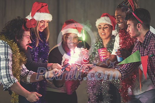 multiethnic group of young happy casual business people lighting a sparkler and having fun while celebrating new year eve in front of concrete wall at new startup office multiethnic group of young happy casual business people lighting a sparkler and having fun while celebrating new year eve in front of concrete wall at new startup office
