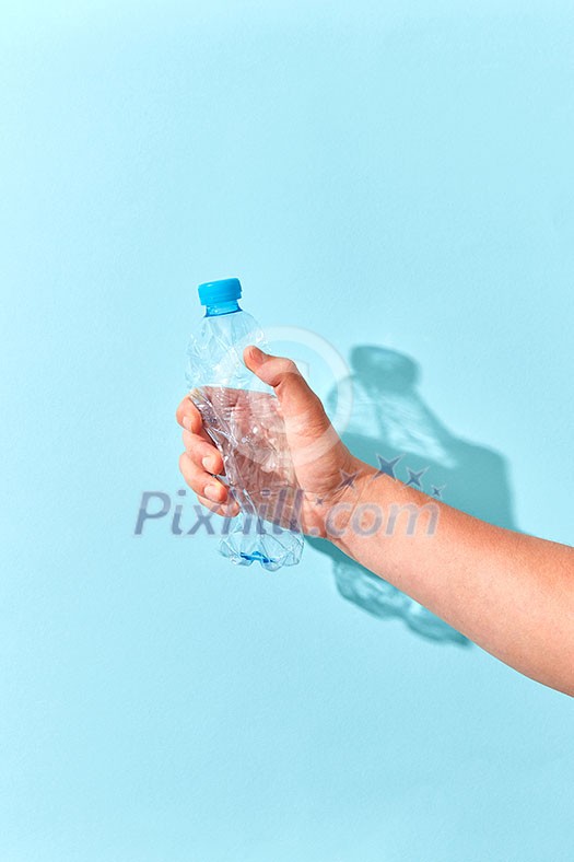 Empty plastic bottle crushed by hand on a pastel blue background with transparent shadows. Place for text. Ecological problem of environmental pollution. Empty plastic bottle crushed by hand on a pastel blue background with transparent shadows. Place for text. Ecological problem of environmental pollution.