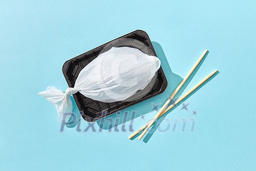 Dinner set of fish from plastic bag served wooden chopsticks with hard shadows on a pastel blue background, copy space. Ecological problem of ocean pollution. Dinner set of fish from plastic bag served wooden chopsticks with hard shadows on a pastel blue background, copy space. Ecological problem of ocean pollution.