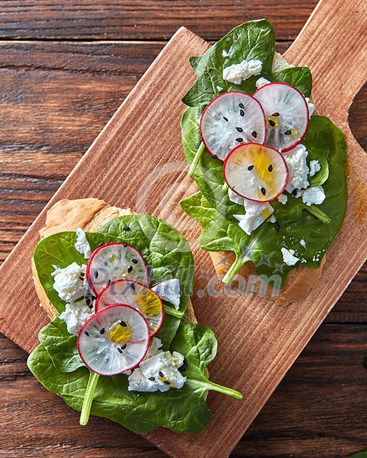 Bruschetta with radishes, spinach and curd cheese with flax seeds on a wooden background, place for text. Healthy natural snack. Flat lay Bruschetta with radishes, spinach and curd cheese with flax seeds on a wooden background, place for text. Healthy natural snack. Flat lay