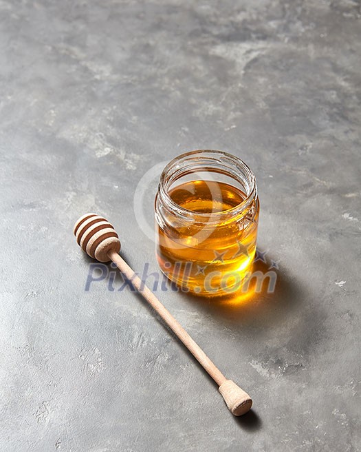 Sweet flower natural honey in a jar and wooden spoon on a gray concrete table, place for text . Rosh hashanah jewish New Year holiday concept. Sweet flower natural honey in a jar and wooden spoon on a gray concrete table, place for text . Rosh hashanah jewish New Year holiday concept.