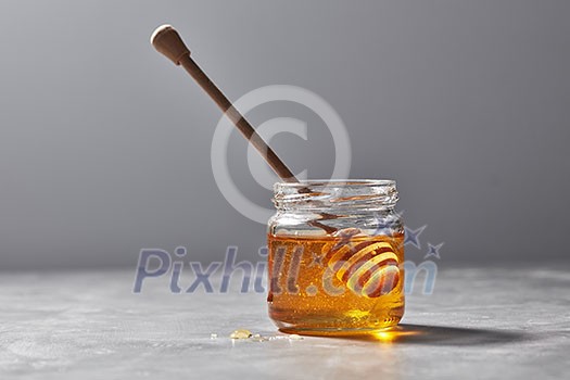 Sweet floral natural honey in a jar and wooden spoon on a gray marble table, copy space. Jewish rosh hashanah holiday concept. Sweet floral natural honey in a jar and wooden spoon on a gray marble table, copy space. Jewish rosh hashanah holiday concept.
