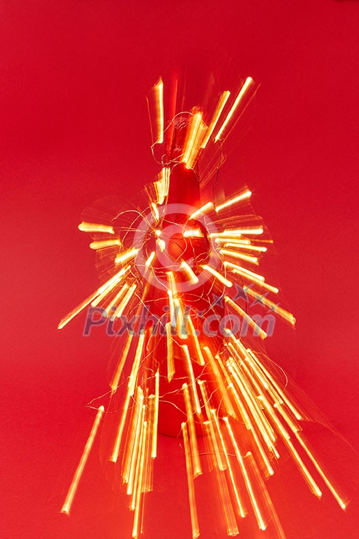 Firecracker from shined trails of Christmas lights on a painted wine bottle on a red background with copy space. New Year congratulation card. Firecracker from shined trails of Christmas lights on a painted wine bottle on a red background with copy space. New Year congratulation card.